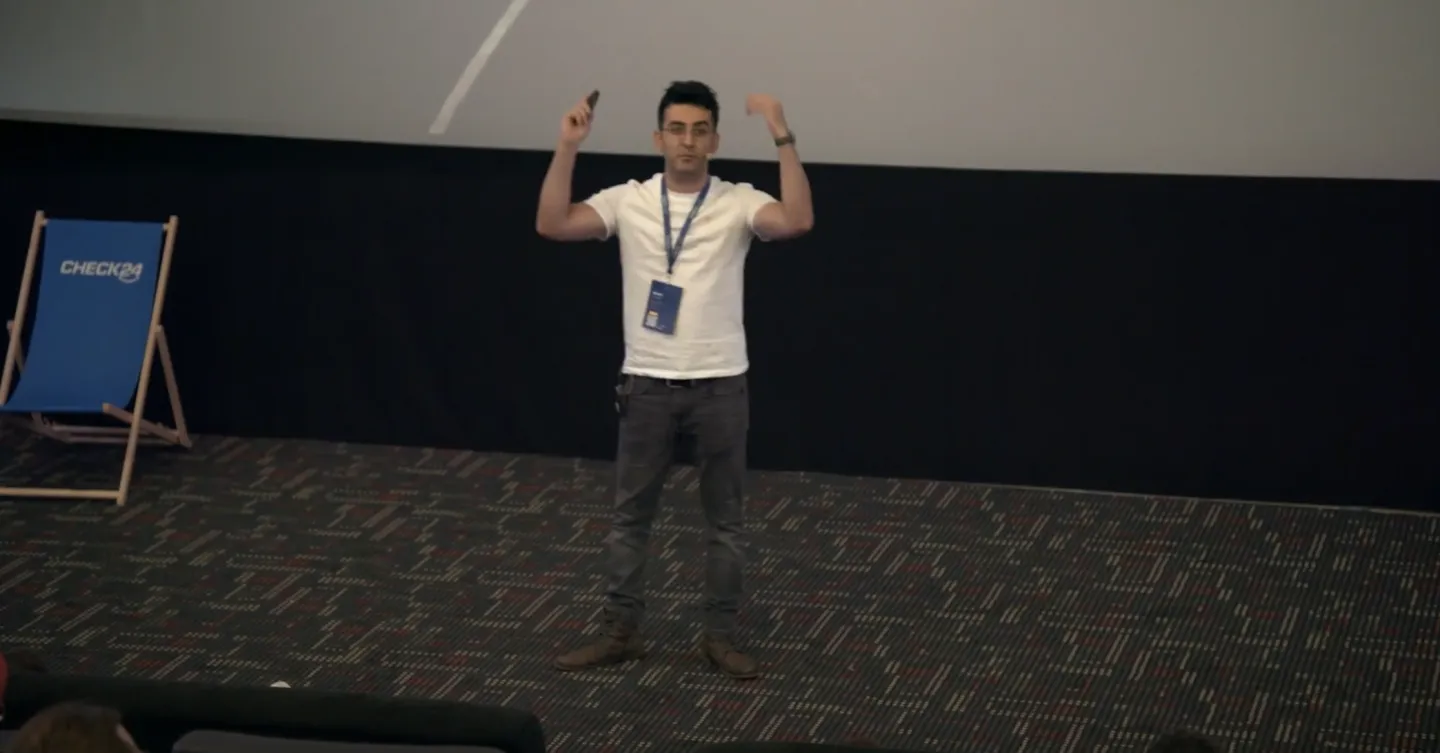 Daniel Daneshi presenting on stage, arms raised, at a conference.